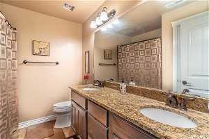 Full size Bathroom with tile floors, toilet, and double vanity, linen closet behind door