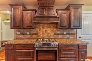 Kitchen featuring tasteful backsplash, granite countertops, stainless steel range with gas stovetop, and premium range hood