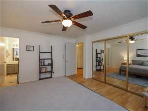 Bedroom featuring light hardwood / wood-style floors, ceiling fan, ornamental molding, a closet, and ensuite bathroom