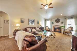 Carpeted living room featuring ceiling fan, high vaulted ceiling, and a tile fireplace