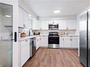 Kitchen with stainless steel appliances, light hardwood / wood-style flooring, white cabinetry, and sink