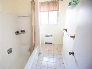 Bathroom featuring radiator, shower / bathtub combination with curtain, and tile flooring