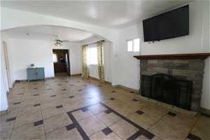 Unfurnished living room featuring tile flooring, ceiling fan, and a stone fireplace