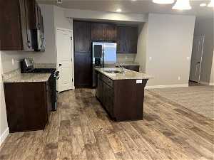 Kitchen featuring sink, hardwood / wood-style flooring, a center island with sink, stainless steel appliances, and dark brown cabinetry