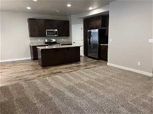 Kitchen with a kitchen island with sink, dark brown cabinets, appliances with stainless steel finishes, a breakfast bar, and dark carpet