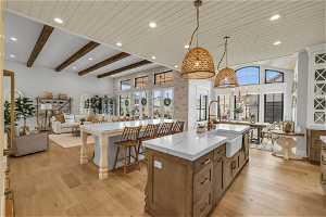 Kitchen with decorative light fixtures, light stone countertops, a center island with sink, light wood-type flooring, and sink