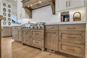Kitchen with tasteful backsplash, premium range hood, white cabinetry, and light hardwood / wood-style flooring