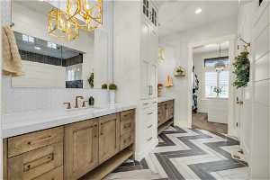 Bathroom with backsplash, parquet floors, vanity, and an inviting chandelier