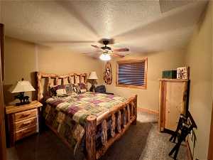 Bedroom with dark colored carpet, a textured ceiling, and ceiling fan