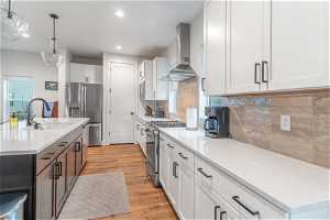 Kitchen with light hardwood / wood-style flooring, stainless steel appliances, wall chimney exhaust hood, tasteful backsplash, and white cabinetry