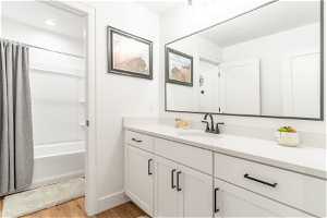 Bathroom with large vanity, hardwood / wood-style flooring, and shower / bathtub combination with curtain