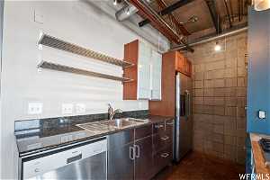 Kitchen with dishwashing machine, tile walls, sink, dark stone counters, and stainless steel refrigerator with ice dispenser
