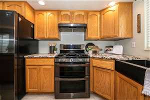 Kitchen featuring black fridge, light stone countertops, and stainless steel gas range