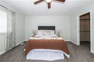 Bedroom with a closet, dark carpet, a spacious closet, and ceiling fan
