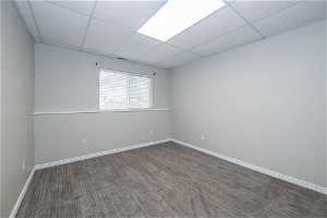 Empty room with dark colored carpet and a drop ceiling