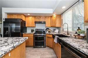Kitchen with stainless steel gas range, light stone counters, black fridge with ice dispenser, dishwasher, and light hardwood / wood-style flooring