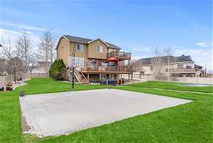 Rear view of property featuring a lawn, a balcony, sport court and a deck