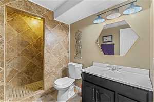 Basement bathroom with vanity, tile walls, tiled shower, tile flooring, and toilet