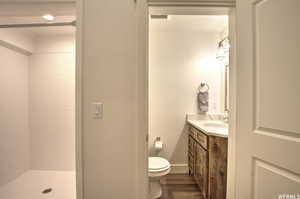 Bathroom with vanity, toilet, hardwood / wood-style flooring, and tiled shower