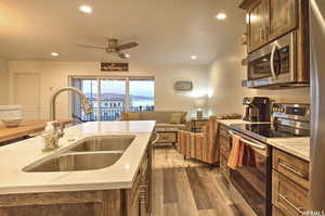 Kitchen with ceiling fan, sink, dark hardwood / wood-style flooring, appliances with stainless steel finishes, and light stone countertops