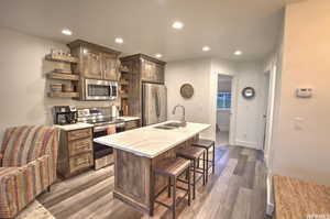 Kitchen with dark hardwood / wood-style floors, sink, stainless steel appliances, a center island with sink, and dark brown cabinets