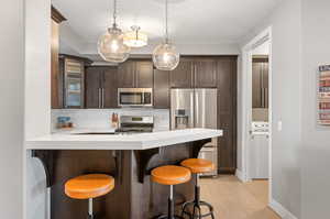 Kitchen with a kitchen breakfast bar, tasteful backsplash, dark brown cabinets, appliances with stainless steel finishes, and hanging light fixtures