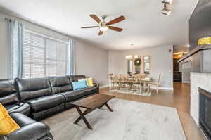 Living room with a textured ceiling, a fireplace, track lighting, and ceiling fan with notable chandelier