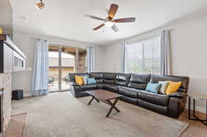 Living room with a textured ceiling, a stone fireplace, and ceiling fan