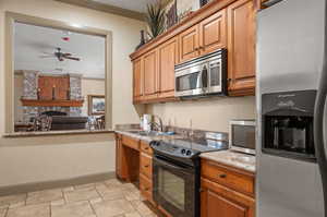 Kitchen featuring granite countertops, a stone fireplace, appliances with stainless steel finishes, and crown molding