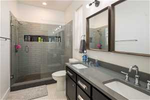 Bathroom with a shower with door, tile floors, dual vanity, and toilet