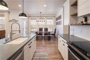 Kitchen with sink, hanging light fixtures, appliances with stainless steel finishes, white cabinets, and light hardwood / wood-style floors