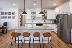 Kitchen featuring hanging light fixtures, wood-type flooring, white cabinetry, and stainless steel appliances