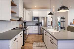 Kitchen featuring sink, hanging light fixtures, white cabinets, stainless steel appliances, and light wood-type flooring