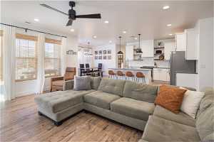 Living room featuring ceiling fan with notable chandelier and light hardwood / wood-style flooring
