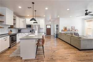Kitchen featuring ceiling fan, pendant lighting, appliances with stainless steel finishes, light hardwood / wood-style flooring, and white cabinetry