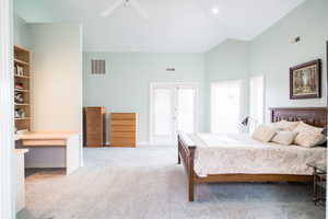 Master Bedroom with high vaulted ceiling, french doors, light colored carpet, Built in Bookshelves and desk and ceiling fan