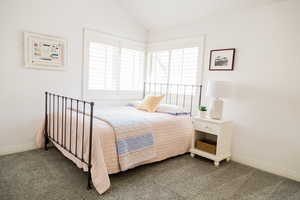 Bedroom with lofted ceiling, dark carpet, and multiple windows