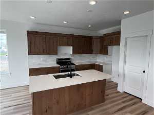 Kitchen featuring backsplash, a center island with sink, stainless steel range with gas cooktop, built in desk, and light wood-type flooring