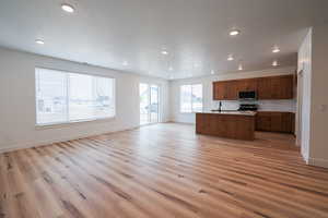 Kitchen with an island with sink, stainless steel appliances, a textured ceiling, light hardwood / wood-style flooring, and sink