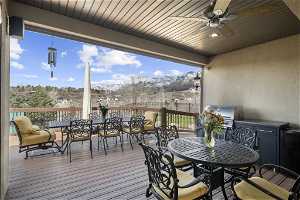 Wooden terrace featuring grilling area, an outdoor kitchen, a mountain view, and ceiling fan