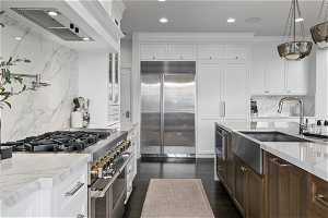 Kitchen with pendant lighting, light stone counters, white cabinets, backsplash, and high quality appliances