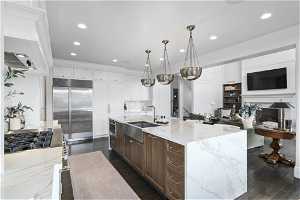 Kitchen featuring decorative light fixtures, a kitchen island with sink, built in fridge, white cabinets, and dark hardwood / wood-style flooring