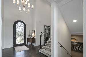 Foyer featuring ornamental molding, a notable chandelier, a towering ceiling, and dark hardwood / wood-style flooring