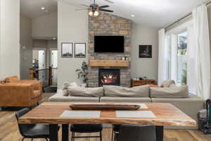 Living room featuring light hardwood / wood-style floors, ceiling fan, vaulted ceiling, and a fireplace