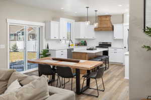 Kitchen featuring a kitchen island, appliances with stainless steel finishes, white cabinets, premium range hood, and light wood-type flooring