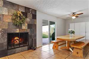 Dining area with ceiling fan, light tile flooring, tile walls, a textured ceiling, and a tile fireplace