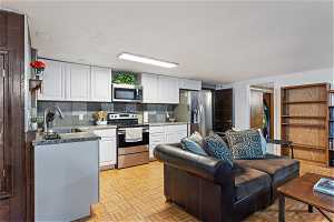 Kitchen with backsplash, sink, stainless steel appliances, white cabinets, and light parquet floors