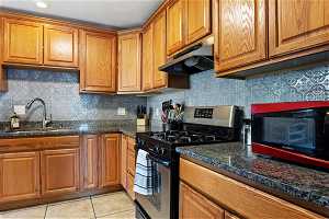 Kitchen with stainless steel range with gas cooktop, tasteful backsplash, light tile floors, and dark stone countertops