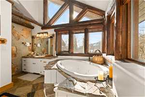 Primary bathroom featuring high vaulted ceiling, oversized vanity, a bathing tub, tile walls, and tile floors