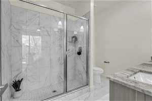 Bathroom with an enclosed shower, vanity, tile flooring, and toilet